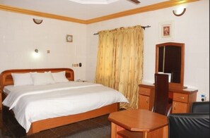A hotel room with a wooden bed, a desk with a chair, a mirror, and a window with curtains.