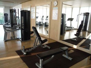 Un gimnasio con diversos equipos de ejercicio, espejos y un reloj en la pared.