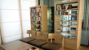 Una biblioteca moderna con estanterías, un área de descanso con sillas y una mesa con un florero.