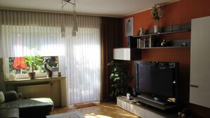 A living room with a sofa, coffee table, TV, and a window with curtains. - Ferienwohnung Em Gardestüffje (Mechernich)