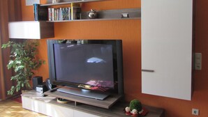 A living room with a flat-screen TV, a white cabinet, a bookshelf, and a potted plant. - Ferienwohnung Em Gardestüffje (Mechernich)
