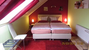 A bedroom with a sloped ceiling, two beds, a chair, and a nightstand with a lamp. - Ferienwohnung Em Gardestüffje (Mechernich)