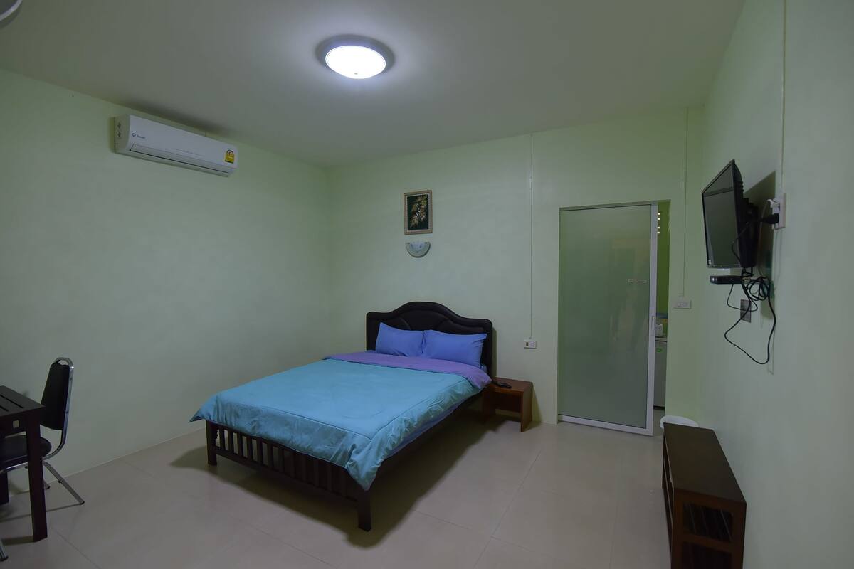 Ein Schlafzimmer mit Bett, Nachttisch, Sessel, Schreibtisch, Fernseher und Klimaanlage.