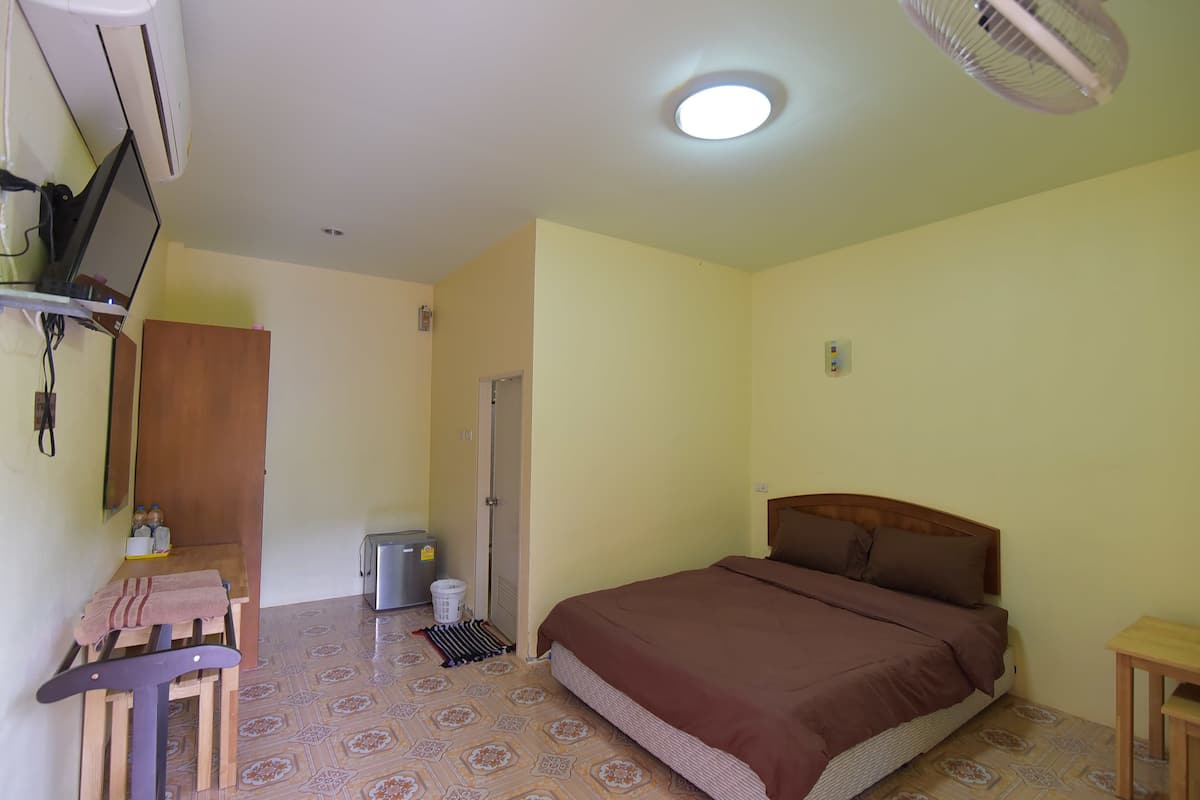 Ein Schlafzimmer mit einem Bett, einem Schreibtisch mit Stuhl, einer Waschmaschine und einem an der Wand befestigten Fernseher.