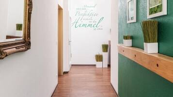 Un pasillo con piso de madera, pared verde con cuadros enmarcados y un espejo a la izquierda.