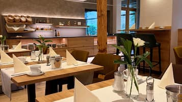Een restaurant met houten tafels, witte tafellinnen en uitzicht op de keuken.