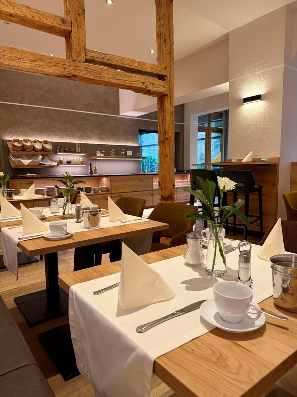 Un restaurante con mesas de madera, manteles blancos y vistas a la cocina al fondo.