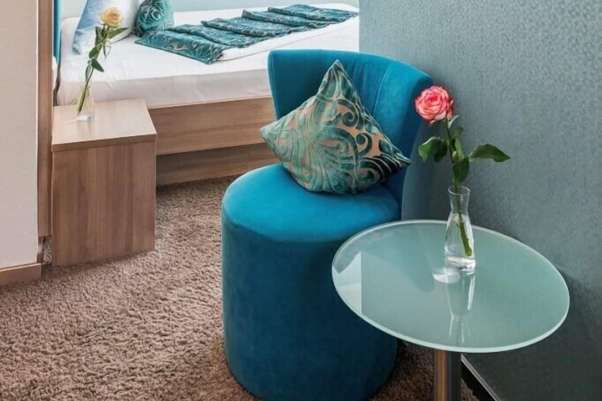Un dormitorio moderno con una cama, una silla azul, una mesita y un florero con una flor.