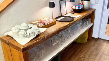 A wooden buffet table with a variety of food items, a potted plant, and a selection of glasses.