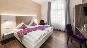 A hotel room with a bed, a desk, a chair, a wardrobe, and a window with curtains.