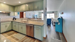 A modern kitchen with green cabinets, a dishwasher, and a large island. - Queen's Grant 211-C | Oceanfront + Sound Views! (Topsail Beach)