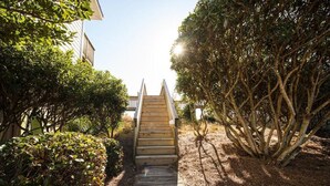 A wooden staircase leading to a building, surrounded by dense foliage and a clear sky. - Queen's Grant 211-C | Oceanfront + Sound Views! (Topsail Beach)