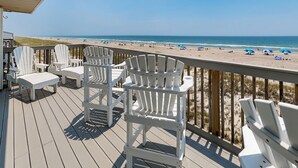 A deck with Adirondack chairs overlooking a beach with umbrellas. - Queen's Grant 211-C | Oceanfront + Sound Views! (Topsail Beach)