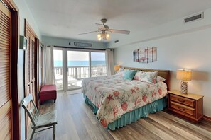A bedroom with a bed, a nightstand, a chair, a ceiling fan, and a view of the ocean.