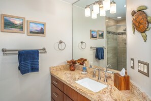 Un baño con encimera de granito, lavabo blanco, espejo y ducha.