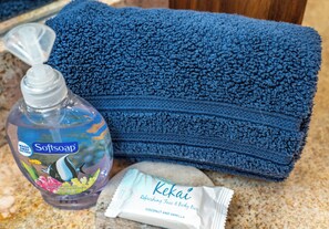 Una botella de jabón líquido, una toalla azul doblada y una pastilla de jabón corporal.