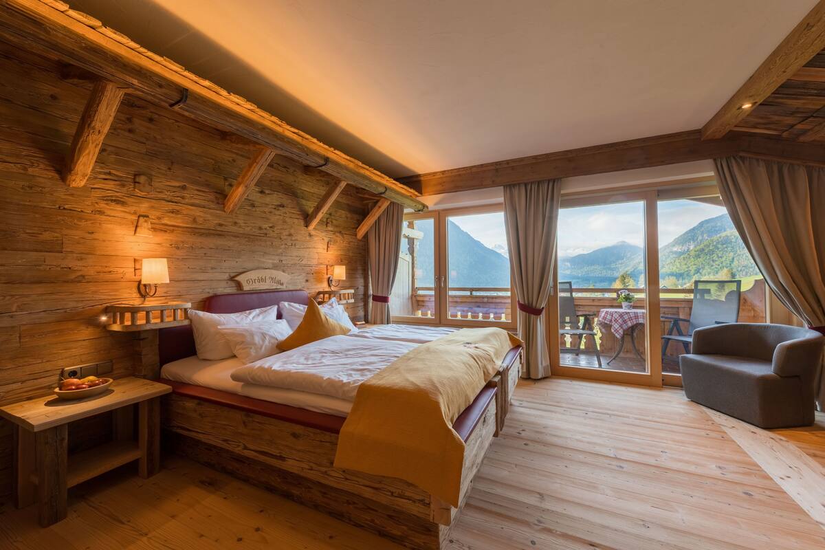 A wooden cabin bedroom with a bed, bedside table, and a view of the mountains.