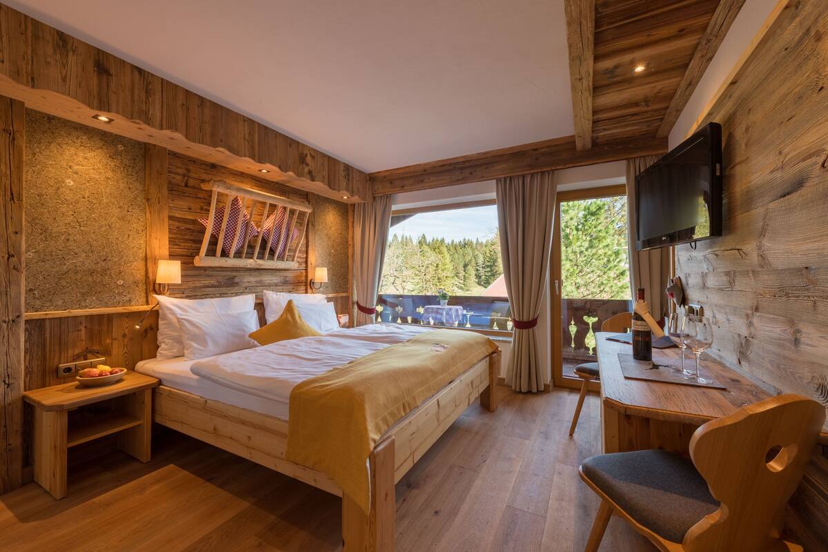A wooden bedroom with a bed, bedside table, and a TV mounted on the wall.
