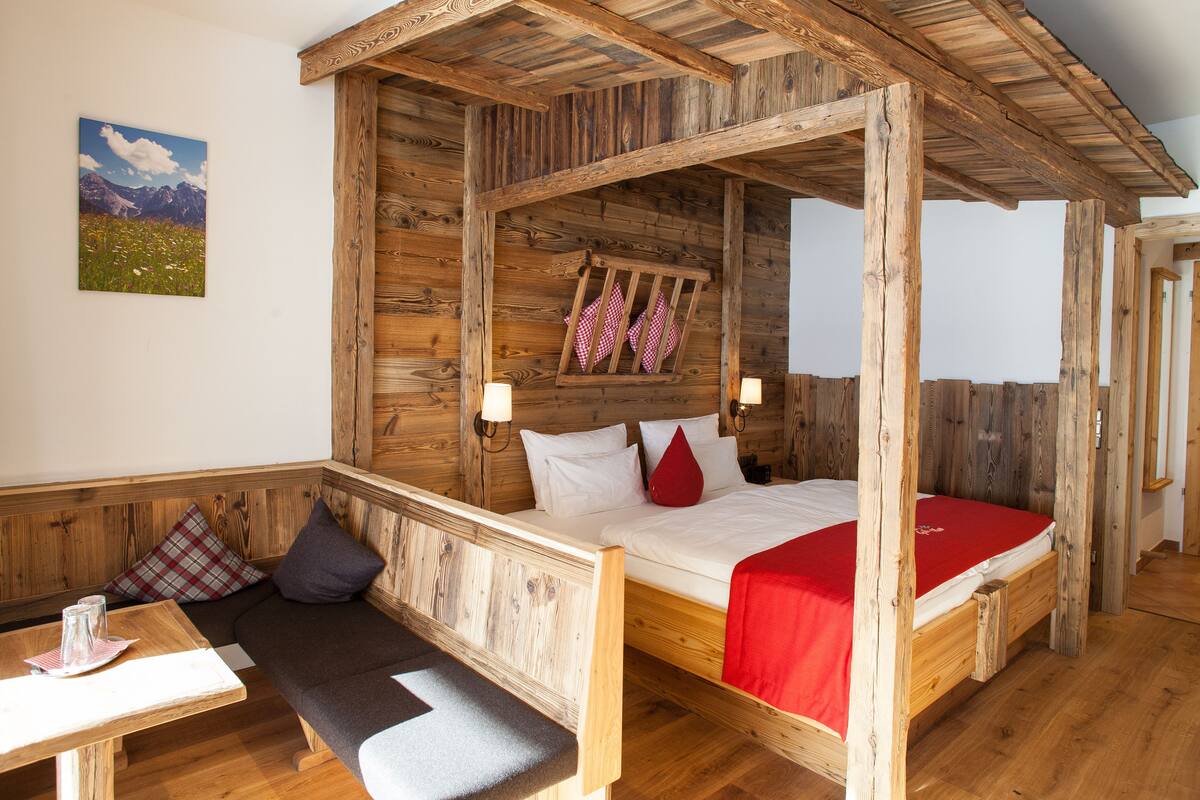 A rustic wooden room with a four-poster bed, a bench, and a table.