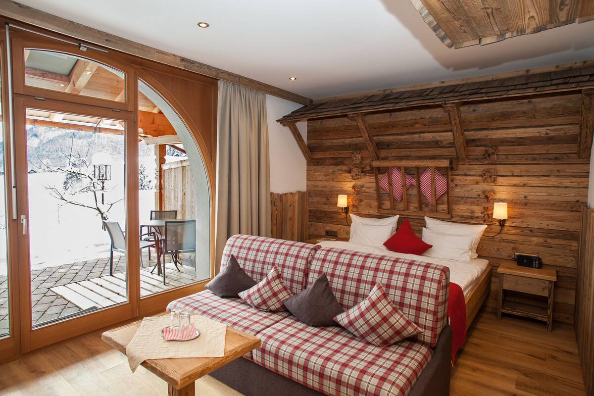 A cozy room with a bed, a sofa, and a table. There is a window with a view of the outside.