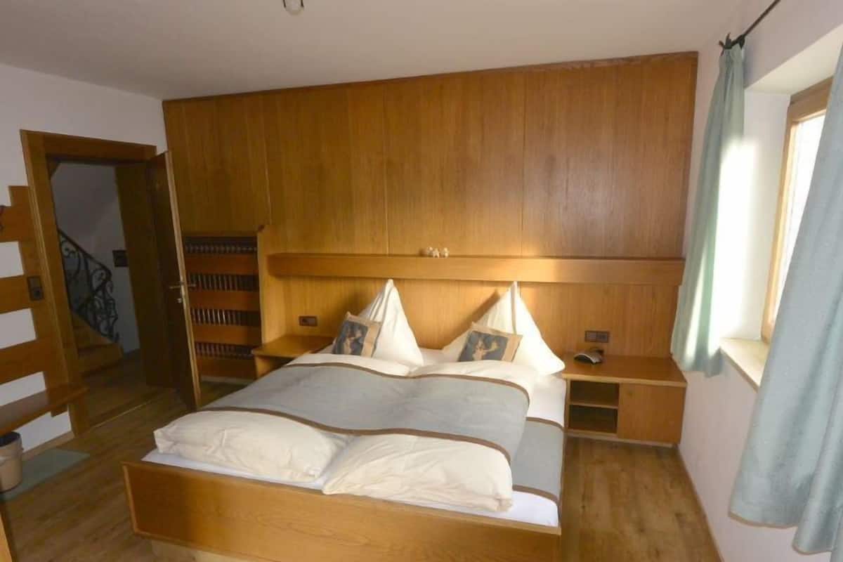 A wooden-framed bed with pillows and a nightstand, a wooden wardrobe, and a staircase.