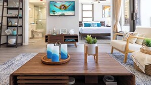 Ein modernes Wohnzimmer mit Couch, Fernseher und Blick ins Schlafzimmer, inklusive einem Holztisch.