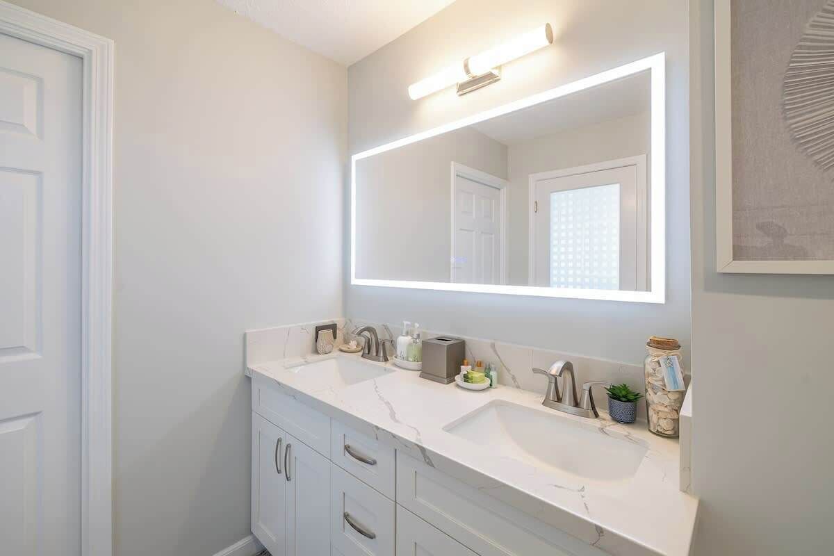 Une salle de bain avec deux lavabos, un grand miroir et un luminaire placé au-dessus du miroir.