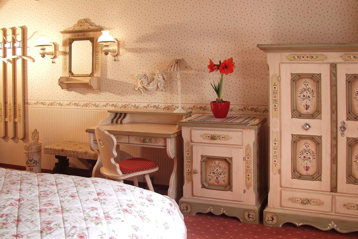 Ein Schlafzimmer mit Bett, Schreibtisch, Stuhl, Kommode und einem an der Wand befestigten Spiegel.
