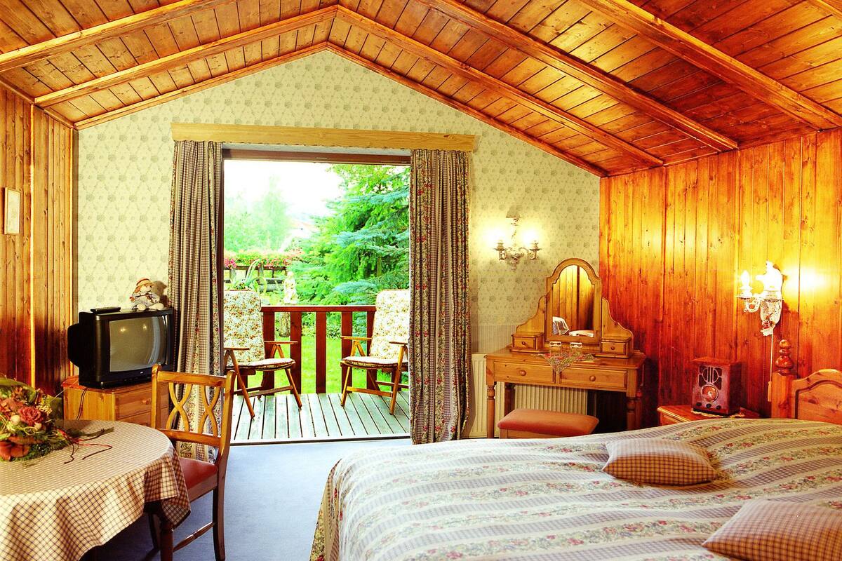 Ein gemütliches Zimmer mit Holzbalkendecke, einem Bett, einem Tisch mit Stuhl, einer Kommode und einem Fernseher.