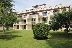 A multi-story building with balconies, a well-maintained lawn, and a large bush in the foreground. - Landhaus & Burg Hotel Romantik (Gotha)
