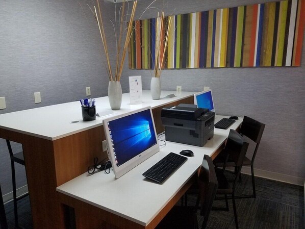 A modern office space with two desks, each equipped with a desktop computer, keyboard, and mouse. There are two vases with decorative sticks on the desks, and a colorful striped wall in the background. - Holiday Inn Express Daytona Beach - Speedway (Daytona Beach)