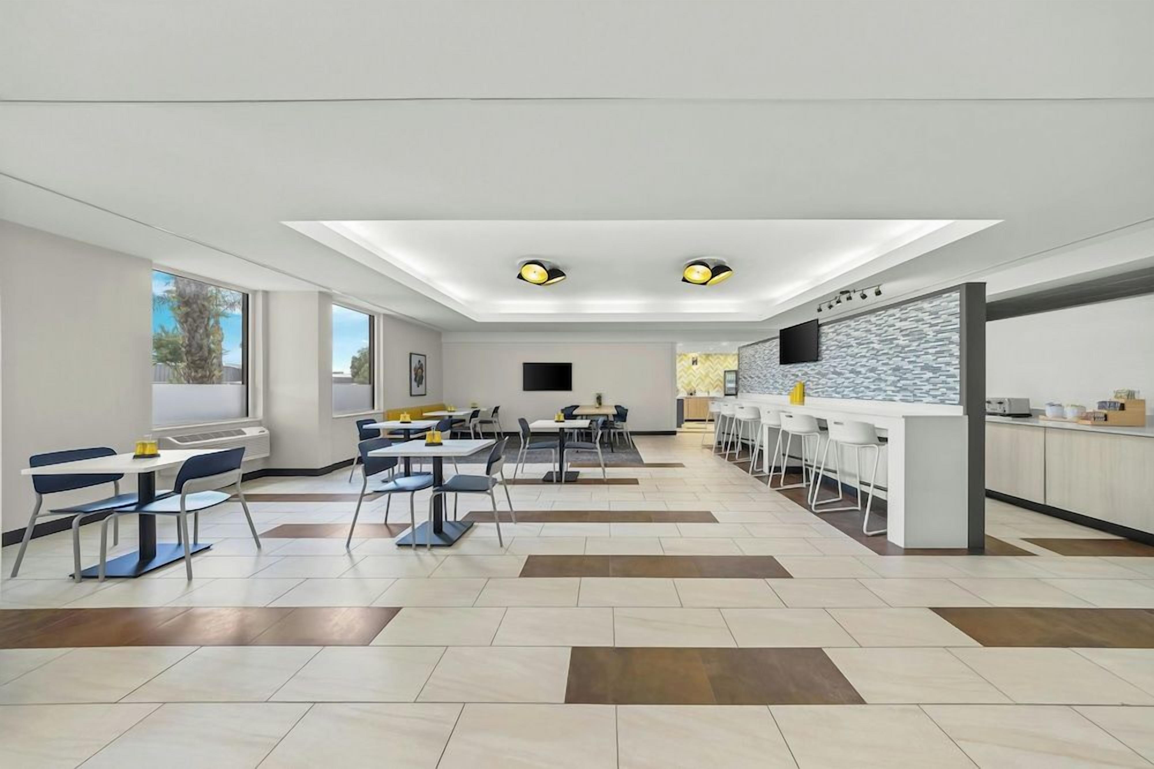 A modern dining area with multiple tables and chairs, a kitchen counter, and a large window providing natural light.