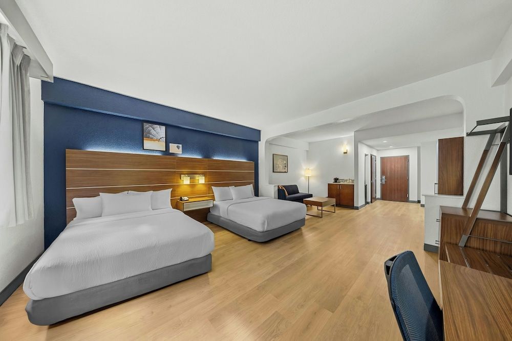 A hotel room with two beds, a desk, a chair, and a staircase.
