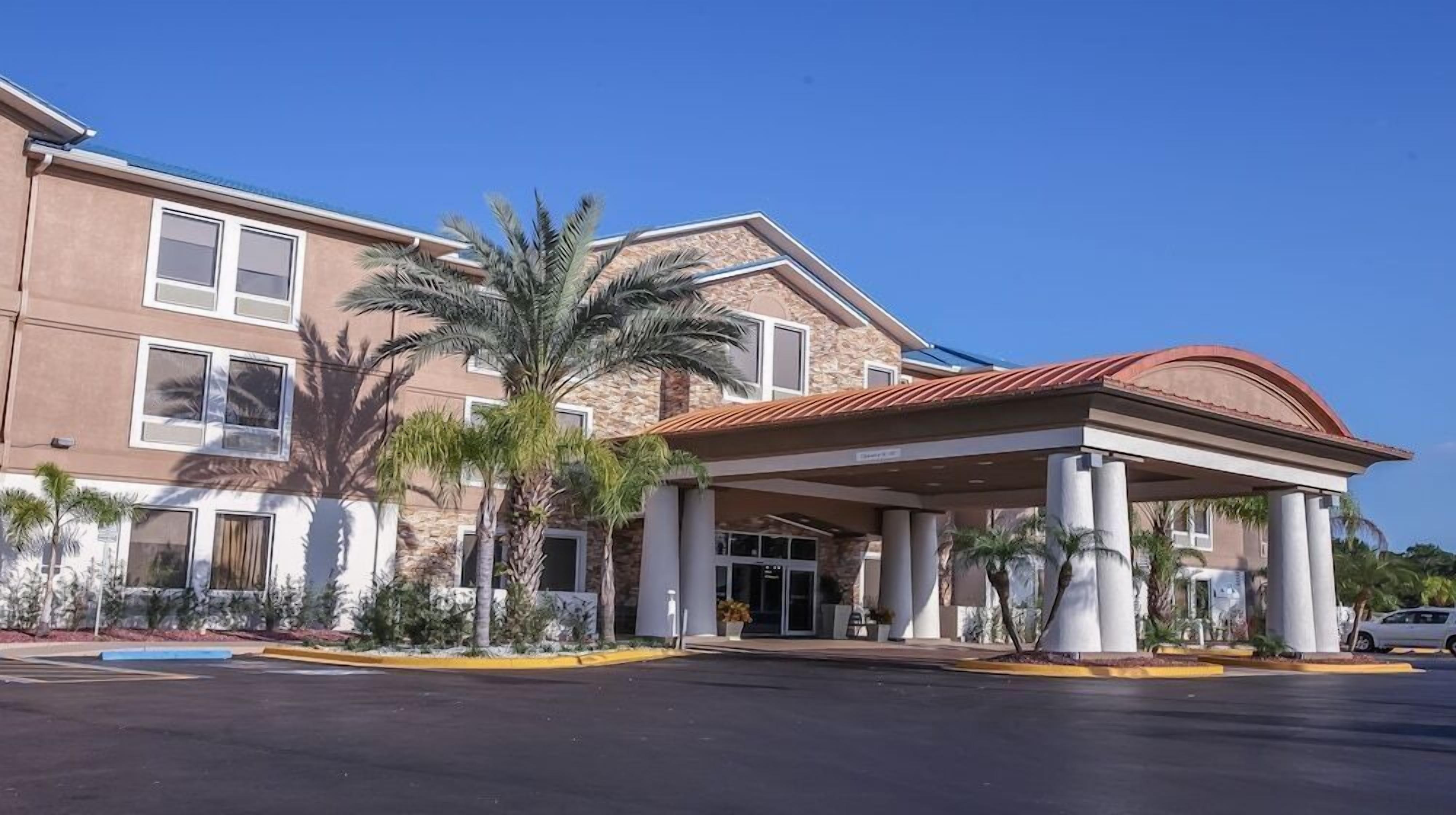 A hotel with a covered entrance, palm trees, and a parking lot.