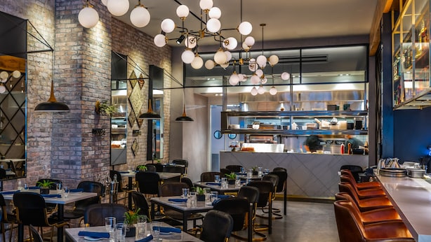 A restaurant interior with brick walls, hanging spherical light fixtures, and a visible kitchen area.