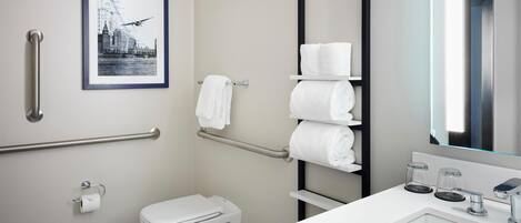 A modern bathroom with a toilet, handrails, a sink with a mirror, and a framed picture on the wall.