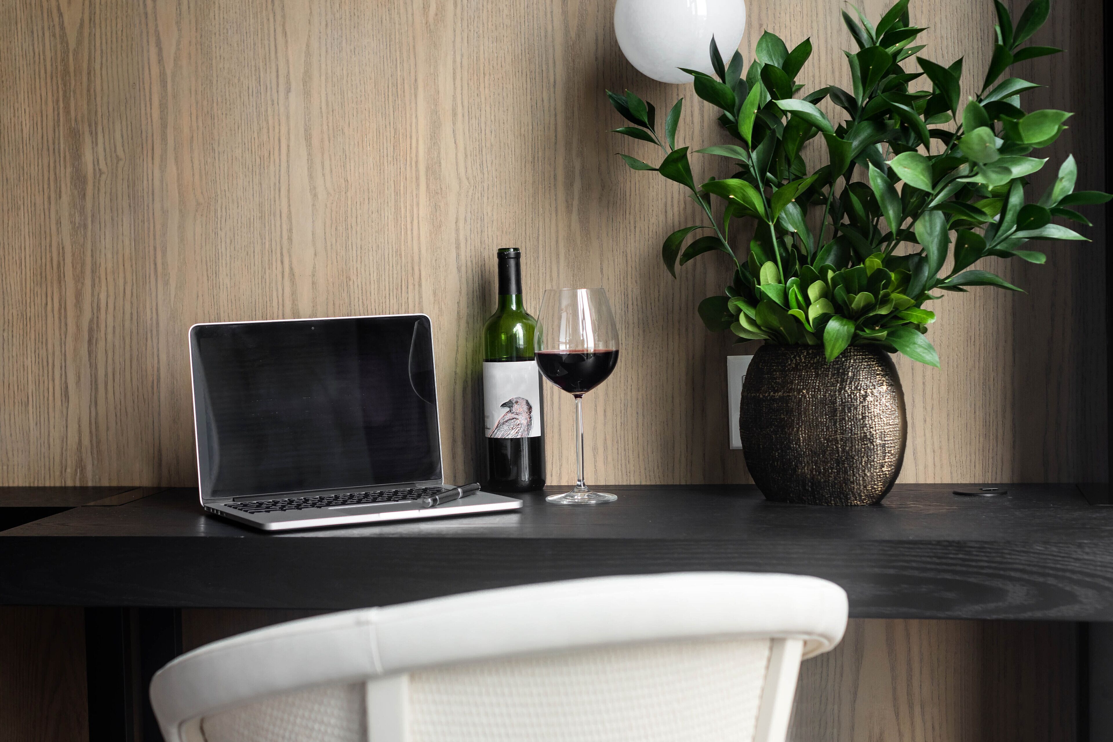 A laptop, a wine bottle, and a glass on a wooden table with a potted plant.