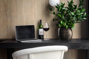 Una computadora portátil, una botella de vino y una copa sobre una mesa de madera con una planta en maceta.
