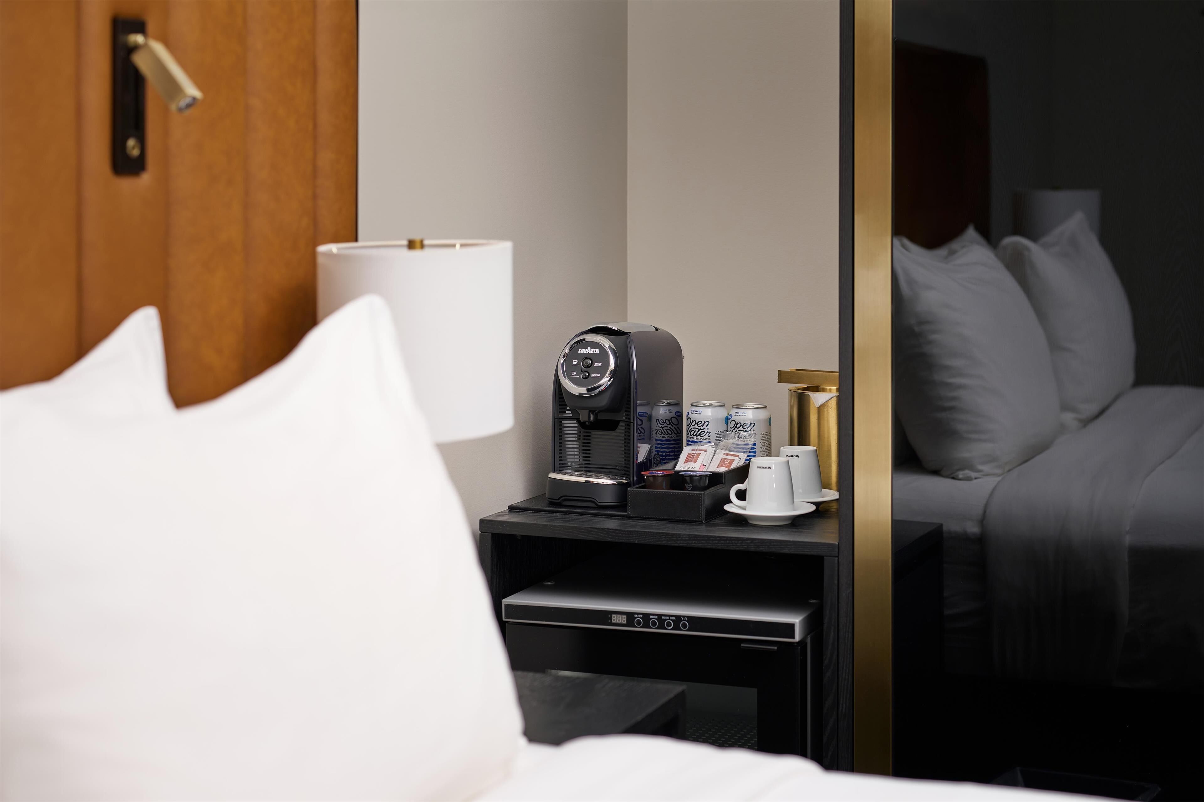 A hotel room with a bed, a nightstand with a coffee maker, a cup, and a remote control.