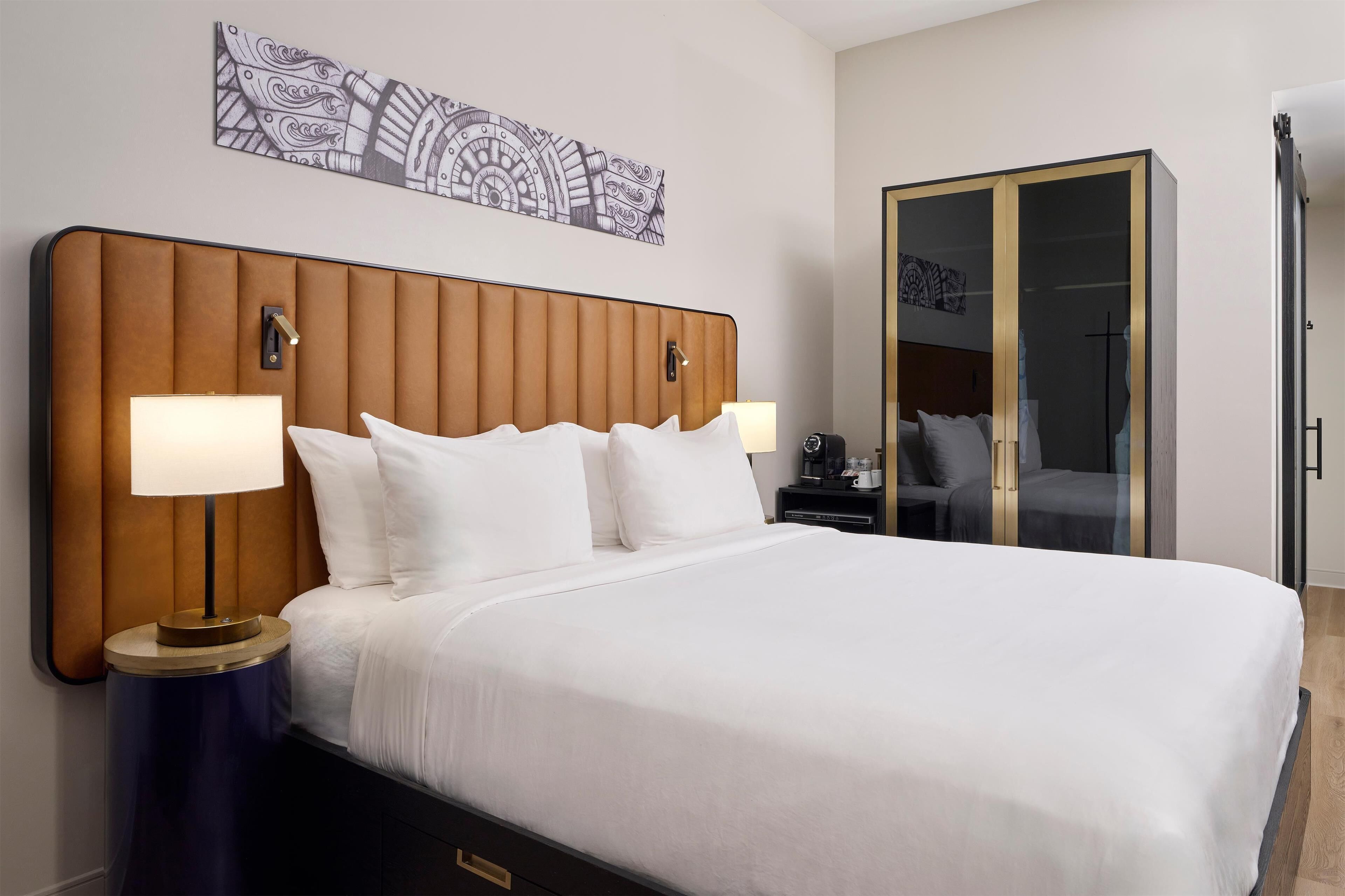 A neatly made bed with white linens and two bedside lamps, a wooden headboard, and a large wardrobe with a mirrored closet door.