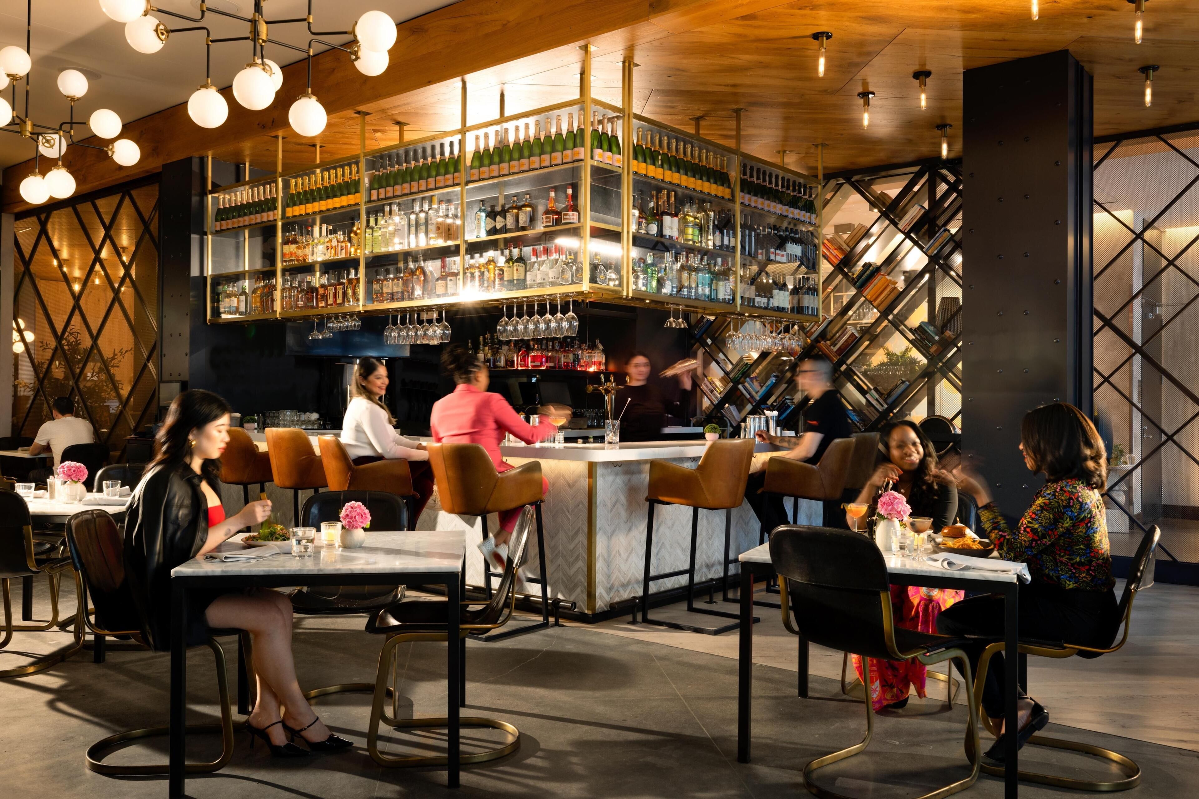A bar area with multiple shelves of bottles and glasses, a bar counter, and seating for patrons.
