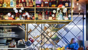 A bar area with multiple shelves of bottles, a bar counter, and three bar stools.