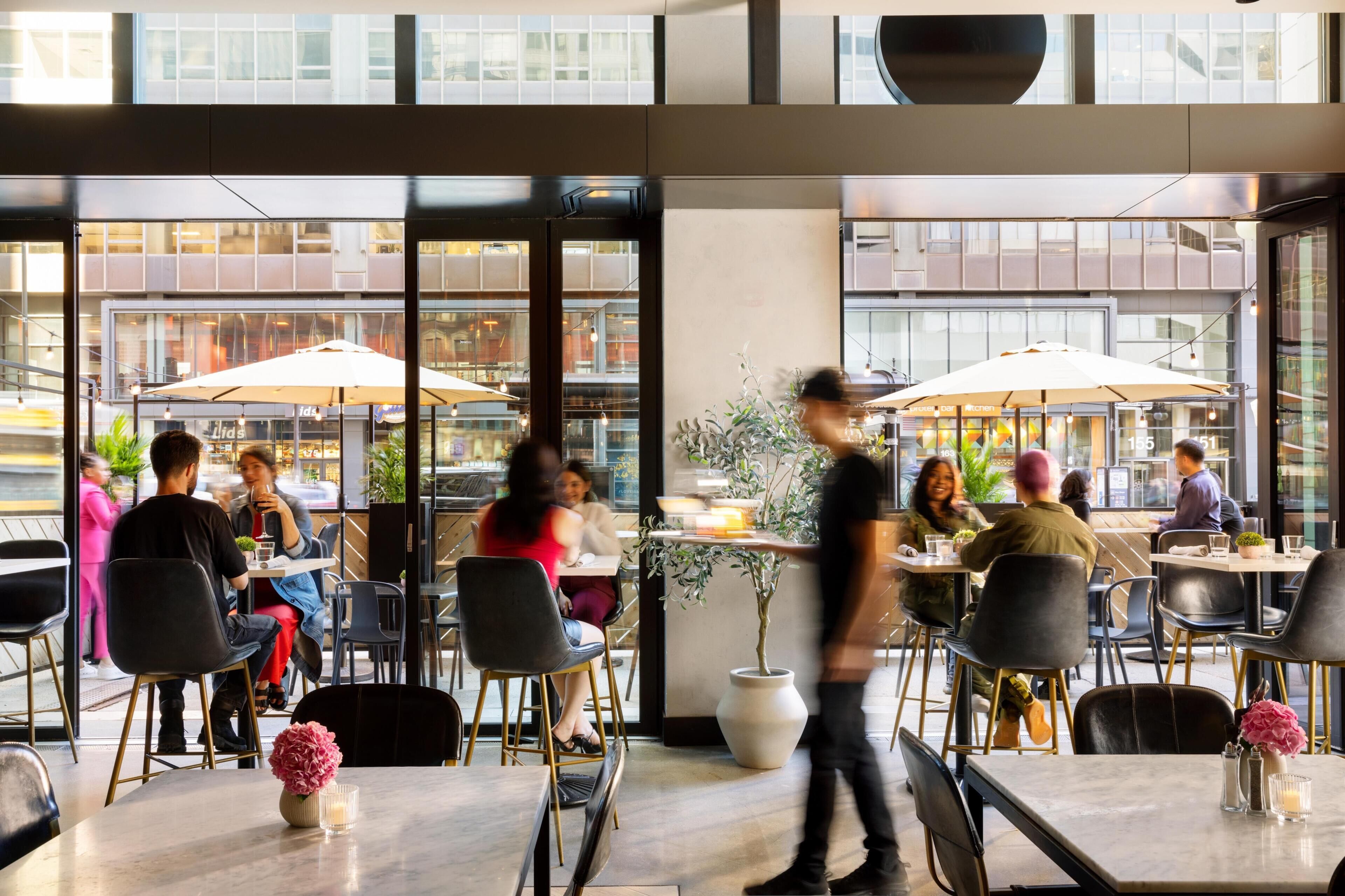 An indoor dining area with tables, chairs, and large windows overlooking a street.