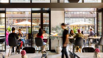 An indoor dining area with tables, chairs, and large windows overlooking a street.
