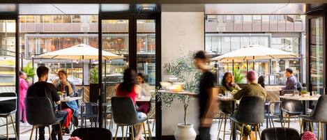 An indoor dining area with tables, chairs, and large windows overlooking a street.