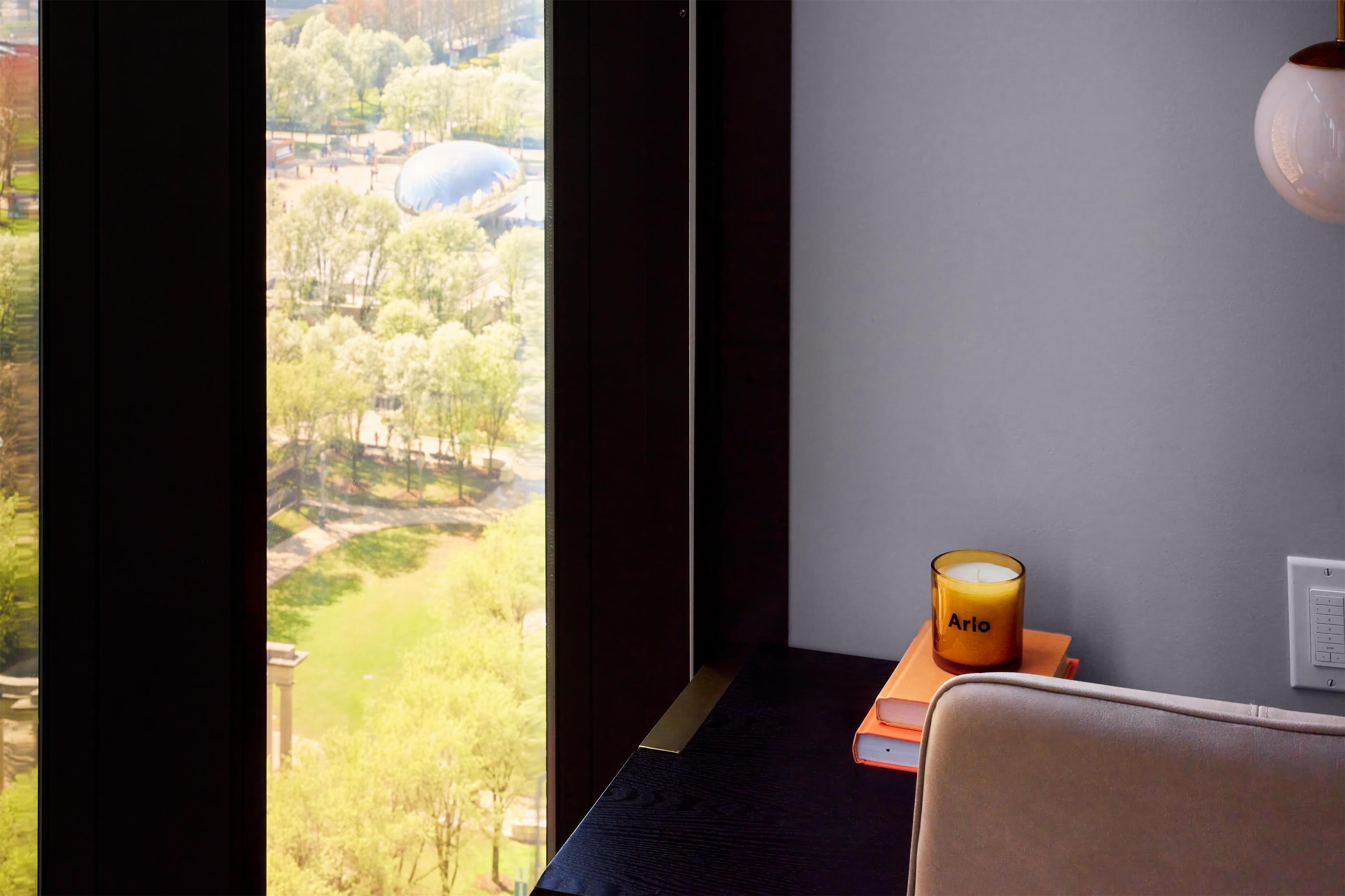 A room with a view of a park, a candle labeled "Arlo" on a table, and a wall socket.
