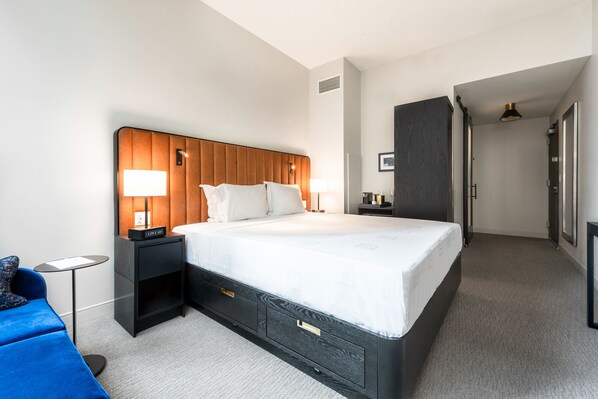 A hotel room with a large bed, bedside tables, a small desk, a chair, and a wardrobe. - Arlo Chicago (Chicago)