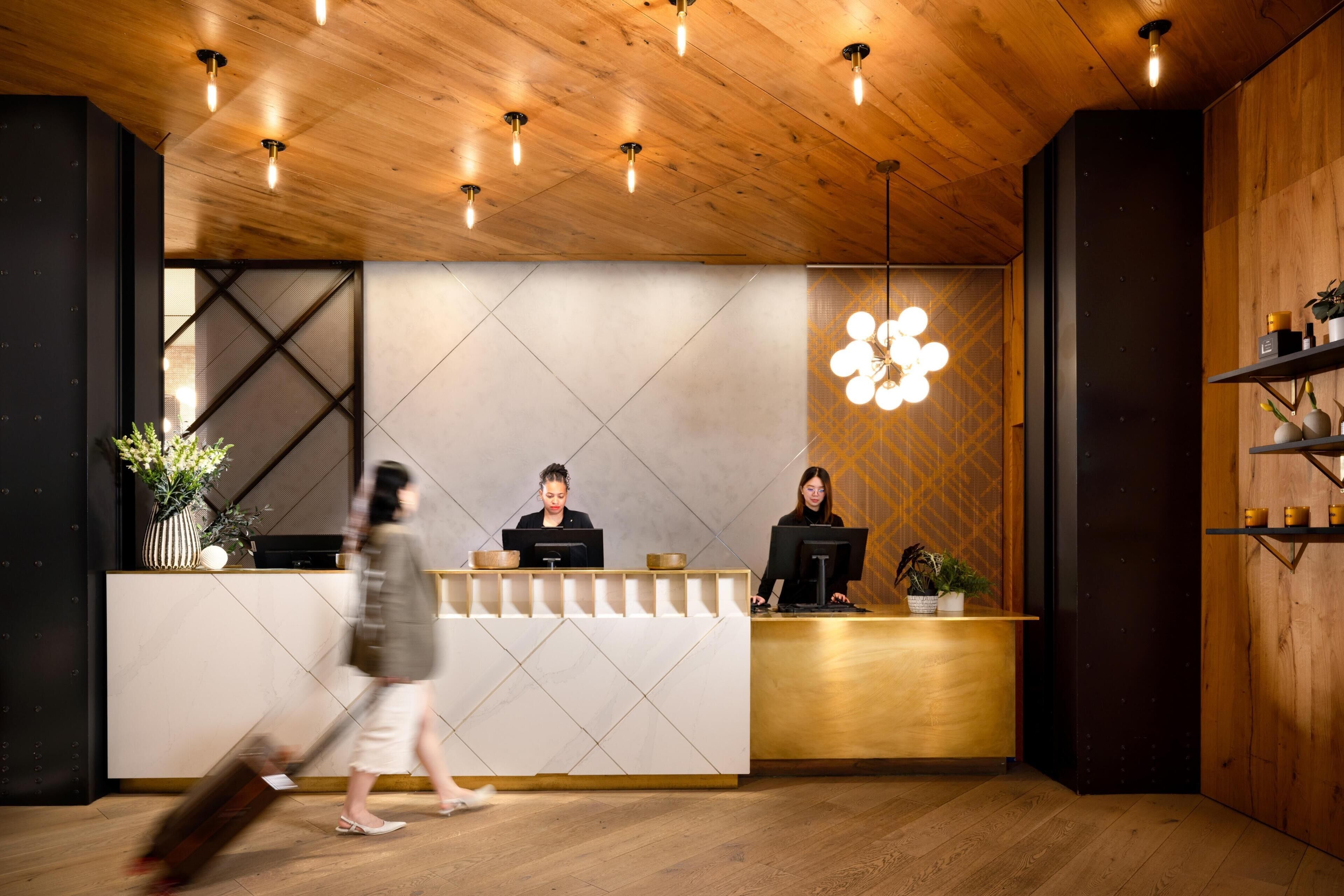 A reception desk with two staff members, a modern light fixture, and a wooden interior.