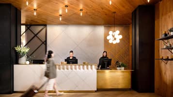A reception desk with two staff members, a modern light fixture, and a wooden interior.