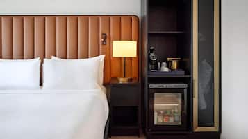 Habitación de hotel con cama, mesita de noche con lámpara, minibar y una obra de arte colgada en la pared.